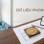 Bản vẽ căn hộ, la bàn phong thủy và máy tính bảng trên bàn gỗ.